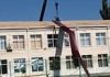 Bungling crane operator sends huge roofing sheets cascading off the top of a school building
