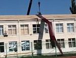 Bungling crane operator sends huge roofing sheets cascading off the top of a school building